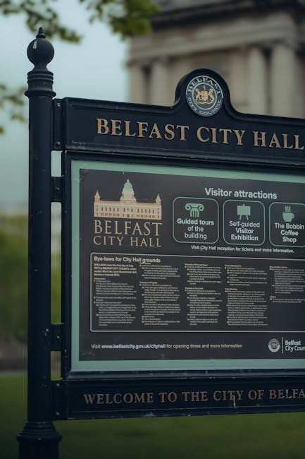 No flowers visible in this image, which depicts a signboard outside Belfast City Hall. The sign features the building's silhouette and information about visitor attractions, guided tours, and events, 